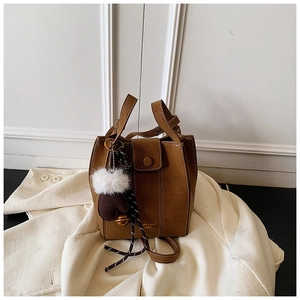 Detail of tan suede bucket bag with top handle and decorative plush charm accessory