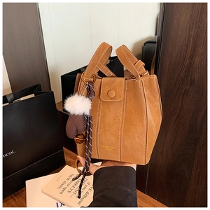 Detail of brown suede bucket bag with contrast stitching and decorative pom-pom charm