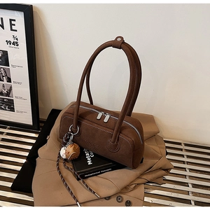 Close-up of brown matte leather cylindrical underarm bag with MUHET logo and baseball charm