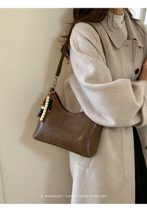 Detail of a brown leather bucket bag with retro bead pendant on a white coat model