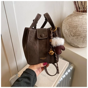 Detail of dark brown matte bucket bag with contrast stitching and golden logo charm