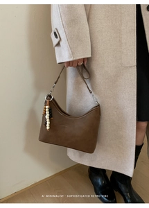 Detail of a brown textured hobo bucket bag with unique tricolor beaded pendant decoration