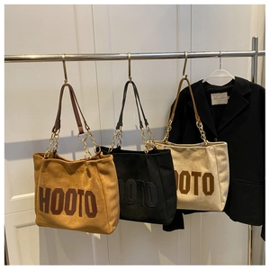 Detail of three HOOTO suede tote bags in brown, black and beige with chain straps
