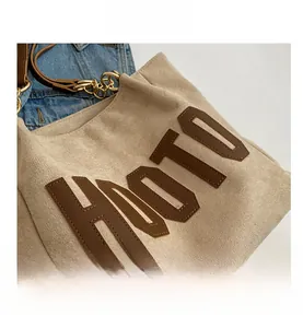 Detail of HOOTO leather letter patch and gold metal hook on beige tote bag