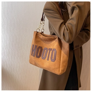 Macro detail of brown suede tote bag featuring a stitched HOOTO patch and chain strap