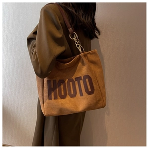 Detail of brown suede tote bag featuring a metal chain strap and retro HOOTO letter patch