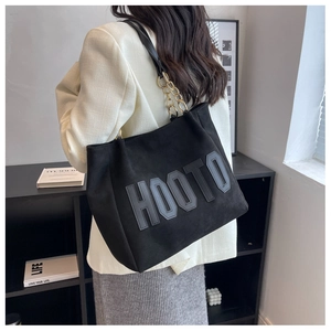 Detail view of black suede tote bag with HOOTO letter patch and metal chain strap