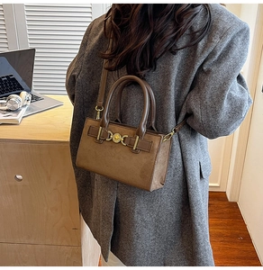 Brown faux suede crossbody bag with gold buckle detail and top handle on office desk