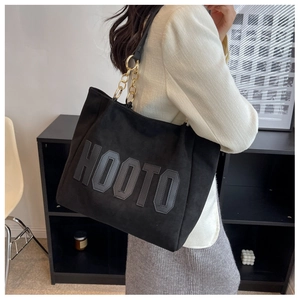 Detail of black suede tote bag with HOOTO lettering and golden metal chain link strap