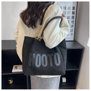 Detail of the black tote bag featuring embossed HOOTO lettering and gold chain strap accent
