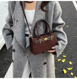 Close-up of a brown suede handbag with gold buckle held by a model in a grey wool coat