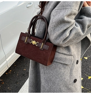 Close-up of a brown suede box bag with gold heart clasp worn with a grey wool coat