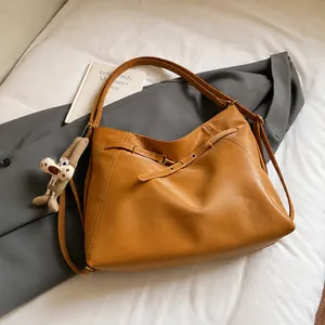 Dettaglio di una borsa hobo in pelle marrone opaca con cinturino e ciondolo di peluche