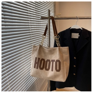 Detail of beige tote bag with HOOTO print, brown leather handles and gold chain strap