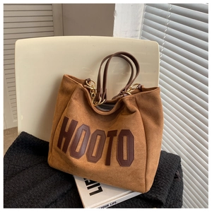 Detail of a brown suede tote bag with HOOTO lettering on a chair in natural light