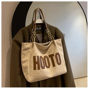 Close-up of beige suede tote bag featuring brown HOOTO lettering and gold chain strap