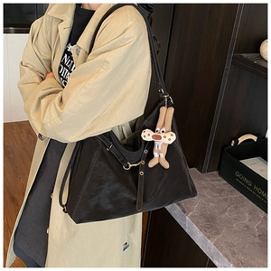 Dettaglio di una grande borsa hobo nera in similpelle con un ciondolo in peluche marrone