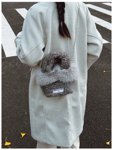Close-up of gray faux fur crossbody bag with silver bead chain on a city street