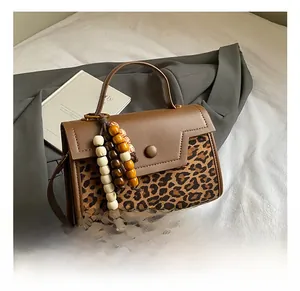 Close-up of leopard print patchwork handbag with geometric flap and colorful bead charm