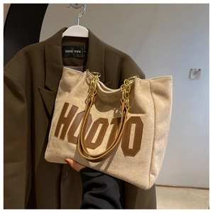 Detail of beige suede tote bag with brown leather handles and gold chain straps