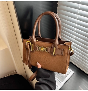 Close-up of brown suede and leather handbag with golden heart buckle and dual handles
