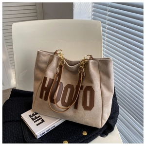Detail of beige tote bag with HOOTO leather patch and gold chain strap on chair