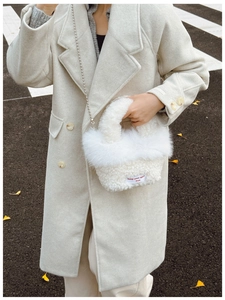Detail of white faux fur handbag featuring silver metal chain and embroidered textile tag
