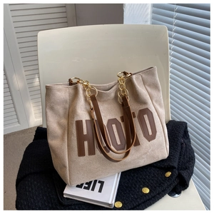 Close-up of beige suede tote bag featuring brown leather straps and gold metal chain links