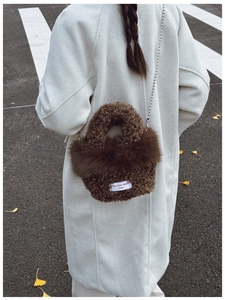 Detail of plush brown teddy crossbody bag with silver bead chain and white quote patch