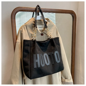 Detail of black tote bag featuring HOOTO embroidery and gold metal chain strap