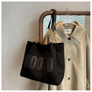 Detail of black HOOTO tote bag with letter applique and metal chain strap on wooden rack