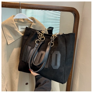Close-up of black suede tote bag with 3D letter detail and gold chain shoulder strap
