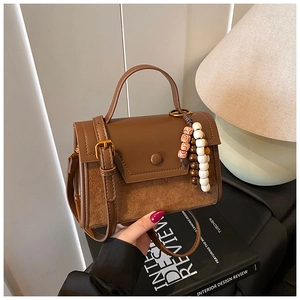 Detail of a brown leather crossbody bag featuring a round buckle and unique wood bead charms