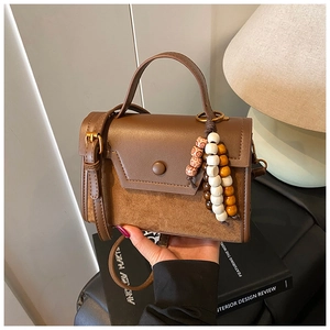 Close-up of brown patchwork leather handbag with vintage pendant and crossbody strap