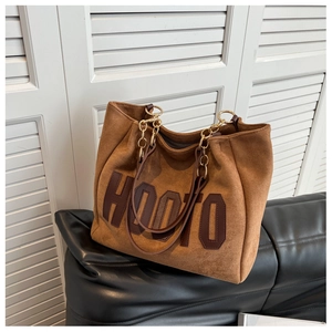 Detail of brown suede tote bag featuring HOOTO lettering and metal chain shoulder strap