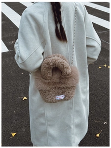 Close-up of brown fuzzy plush shoulder bag featuring a metallic ball chain and woven label
