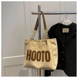 Detail of off-white tote bag with brown HOOTO print and gold metal chain straps