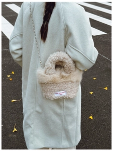 Detail of off-white faux shearling crossbody bag with metal chain strap and fabric label