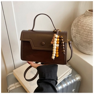 Detail of a brown leather shoulder bag featuring multi-colored wooden bead charm accessories