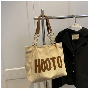 Detail of cream tote bag with brown HOOTO patch and gold chain strap attachment