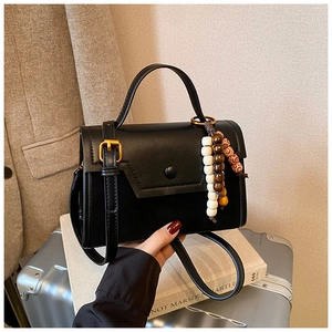 Close-up of black leather handbag featuring round buckle and vintage beaded keychain charm