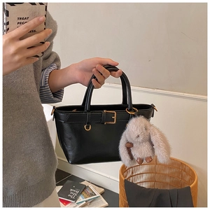 Détail d'un sac à main en cuir noir avec boucle dorée et breloque lapin en peluche