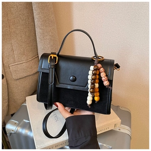 Detail of black crossbody bag with mixed leather textures and colorful wooden bead charms
