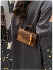 Brown vintage leather crossbody bag with beaded charm accessory in an autumn outdoor setting