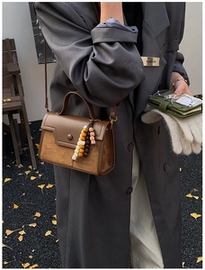 Brown leather and suede crossbody bag with ethnic beaded charm in a cozy autumn street style