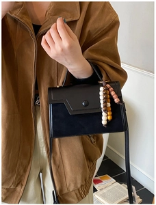 Close-up of black crossbody bag featuring unique wooden bead fringe and metal clasp detail