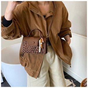 Detail of trendy leopard print crossbody bag featuring brown leather trim and wooden bead charm