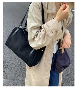 Dettaglio di una borsa Boston in camoscio nero con finiture in pelle indossata con un trench