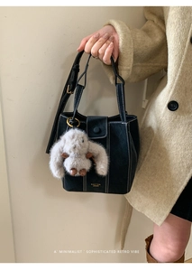 Detalle de bolso negro de ante con costuras blancas y colgante de conejo de peluche