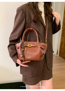 Close-up of brown leather bucket bag featuring gold hardware and vintage charms